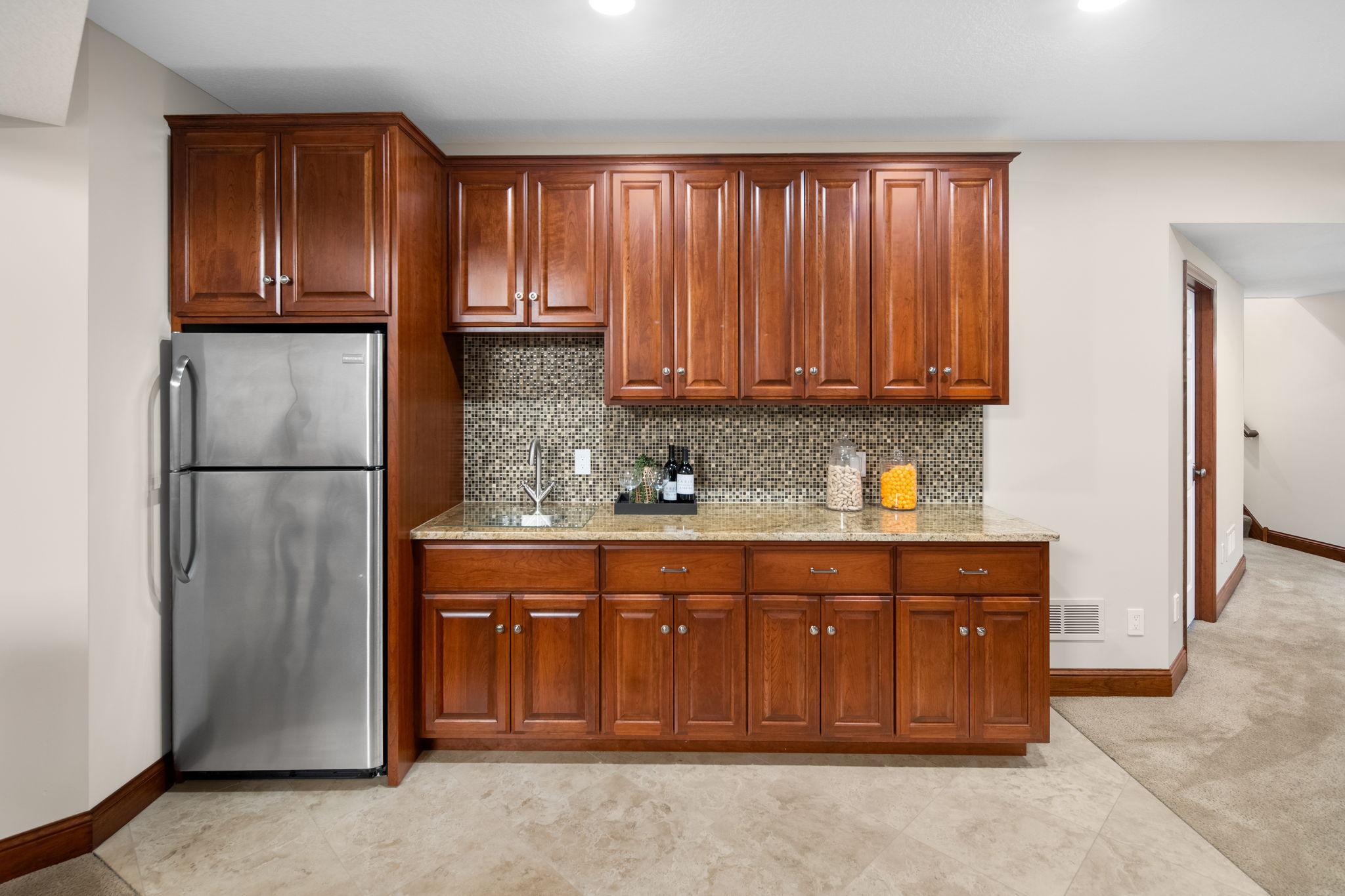 Wet bar with tile backsplash and full-size refrigerator.