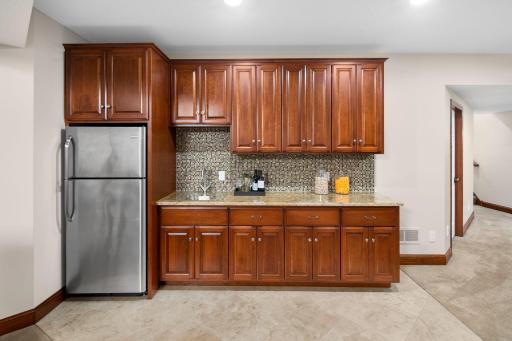 Wet bar with tile backsplash and full-size refrigerator.