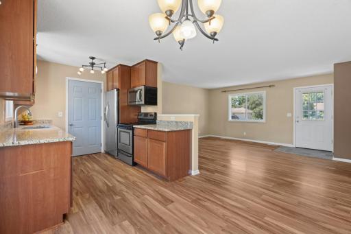 Open dining space and kitchen at 16860 Foliage Ave W featuring wood-look plank flooring, a classic hanging light fixture, raised breakfast bar peninsula, and rich wood cabinetry with stainless steel appliances.