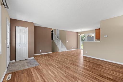 Open-concept main floor at 16860 Foliage Ave W featuring low-maintenance wood-look plank flooring, a neutral accent wall, contemporary staircase railing, and seamless flow toward the dining and kitchen areas.