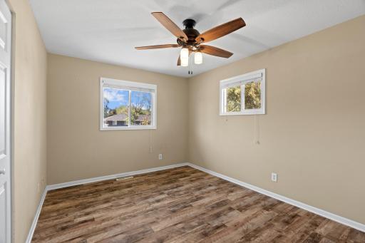 Spacious primary bedroom at 16860 Foliage Ave W featuring low-maintenance plank flooring, dual picture windows for cross ventilation, neutral wall tones, and an integrated ceiling fan with light kit.