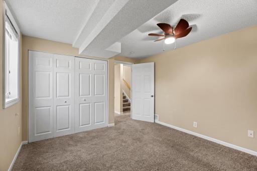 Bright bedroom at 16860 Foliage Ave W featuring neutral carpeting, double bi-fold closet doors, an overhead ceiling fan, and open views leading out to the hallway staircase.