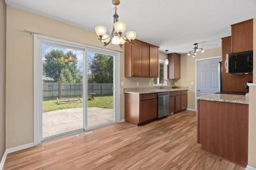 Sunlit dining area and kitchen transition at 16860 Foliage Ave W featuring a traditional hanging chandelier, dark cabinetry with stainless steel appliances, and sliding glass patio doors opening to the private backyard.