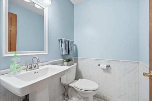 Updated main level Powder Room/Half Bathroom with tile marble like floors and half walls, pedestal sink and updated lighting/mirror