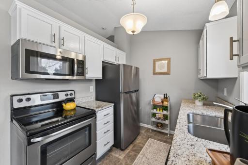 The galley-style kitchen offers crisp white cabinetry, stainless steel appliances, and hard-surface countertops.