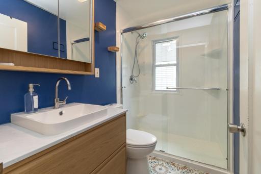 Beautifully updated bathroom with step in shower, new elements and a maintenance free floor! Even this window is new! Be sure to check out the LIGHTED mirror! Updated shower in 2023 and floor, vanity, elements in 2025.