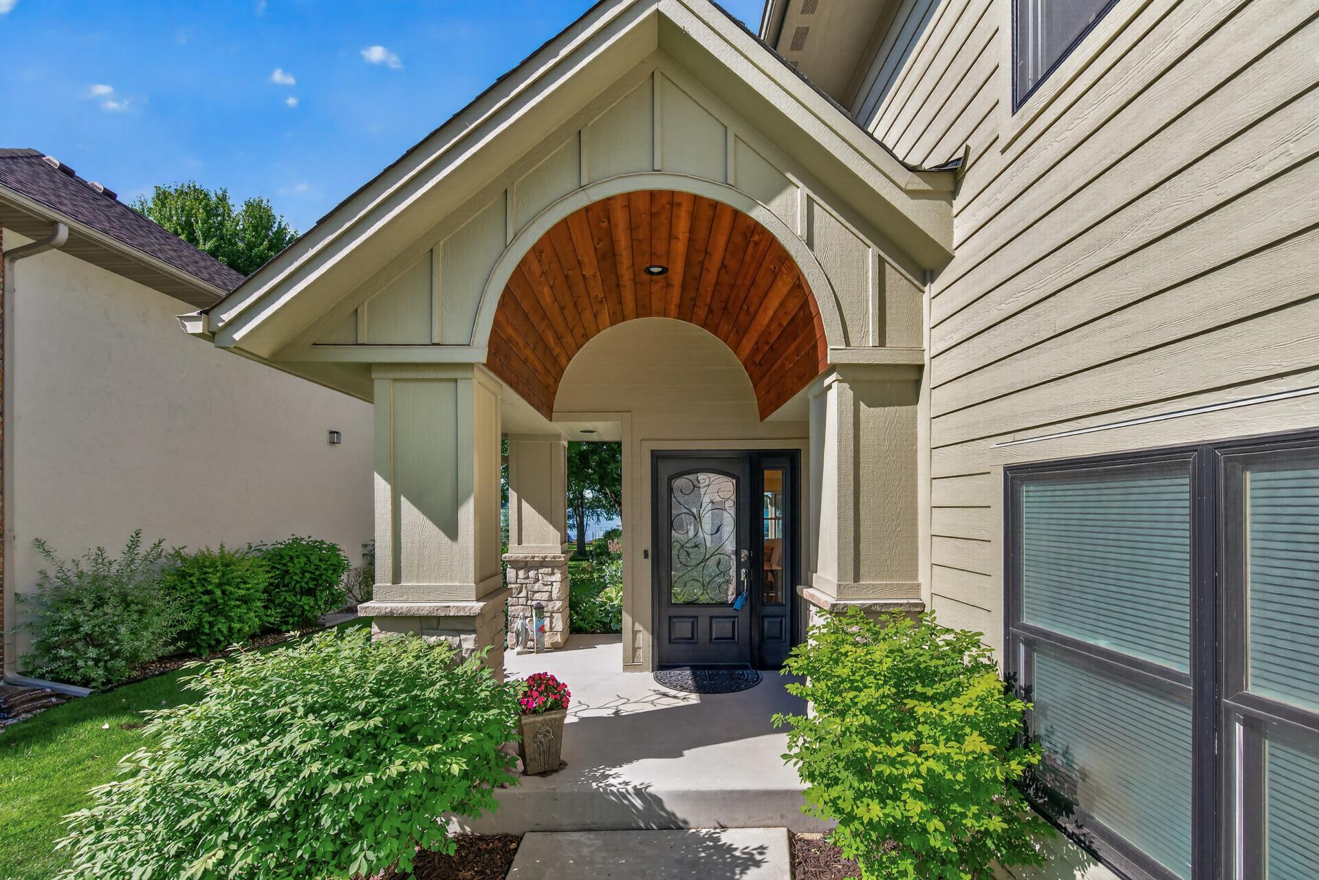 The inviting covered entry offers a custom wood archway, stone-accented columns, and an elegant front door.