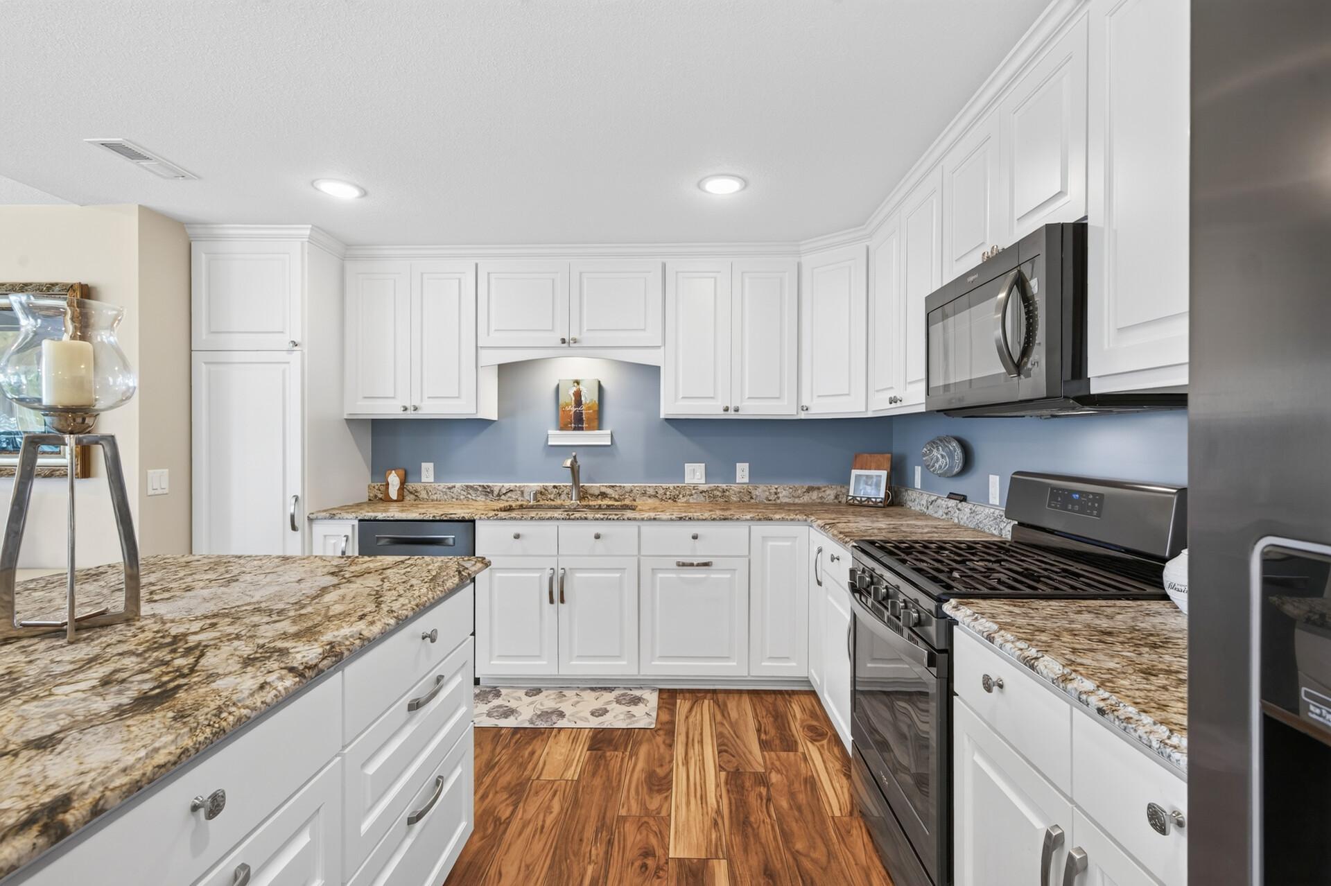 The kitchen offers leathered granite countertops and classic, soft-close white cabinetry.
