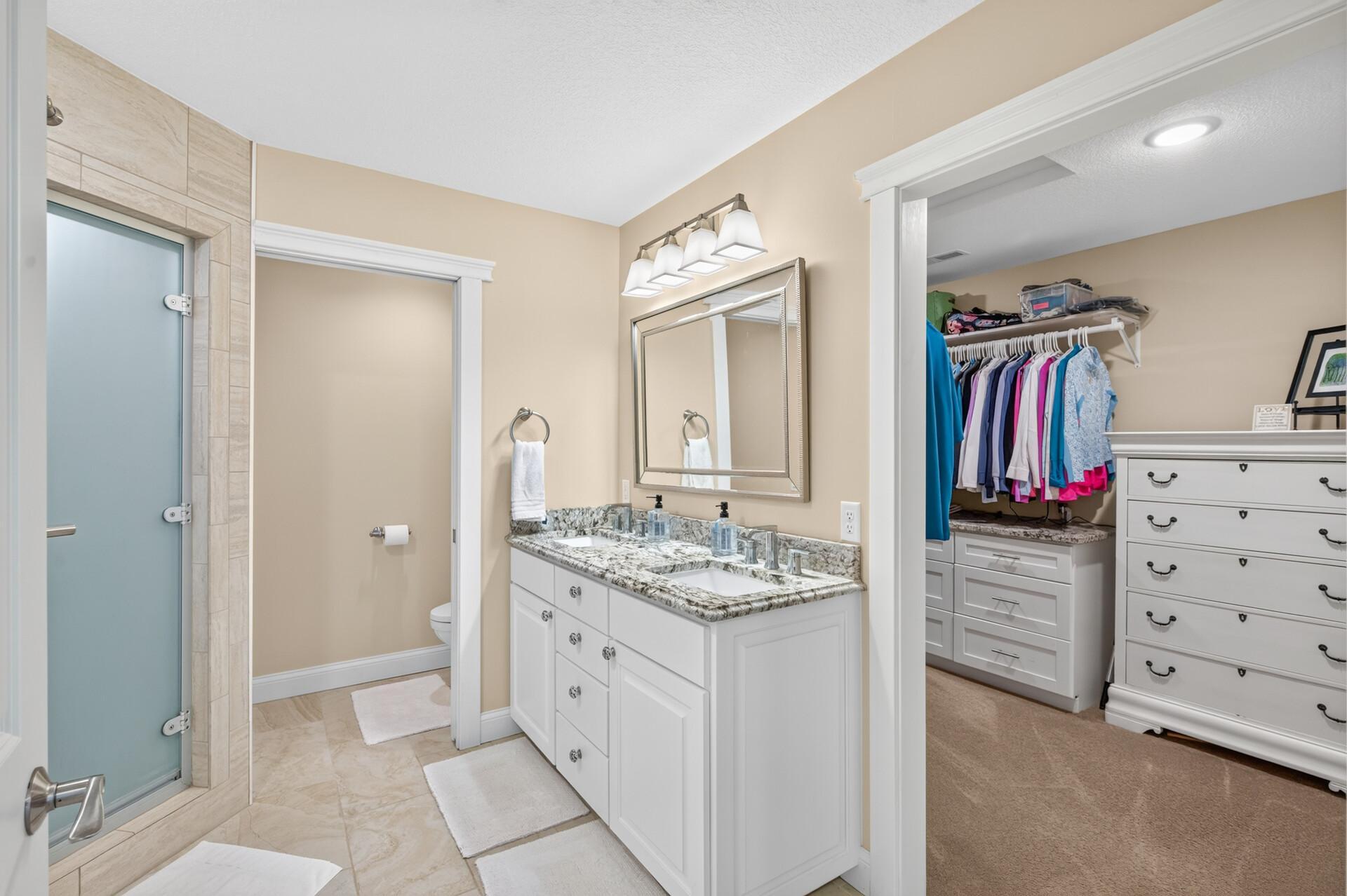 The primary en-suite bathroom features a dual sink vanity with leathered granite countertops, tiled walk-in steam shower, private water closet, and a spacious walk-in closet.