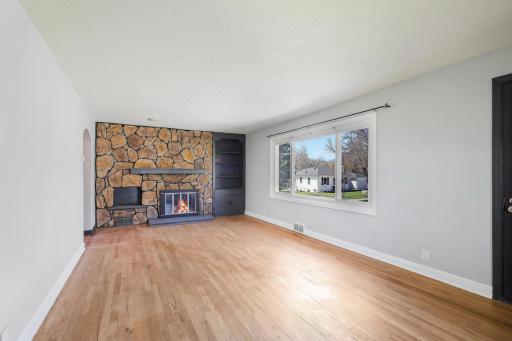 Rear facing living room with hardwood floors and wood burning fireplace.