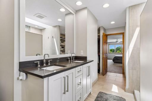 The primary bathroom has been remodeled filled with updates. It has a walk-in tiled shower, tile flooring, custom built-in storage with pull-out drawers, and dual walk-in closets.
