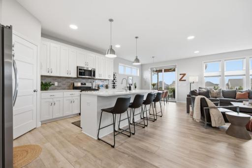 Gracious kitchen with white cabinetry, quartz counters, tiled backsplash, corner pantry.