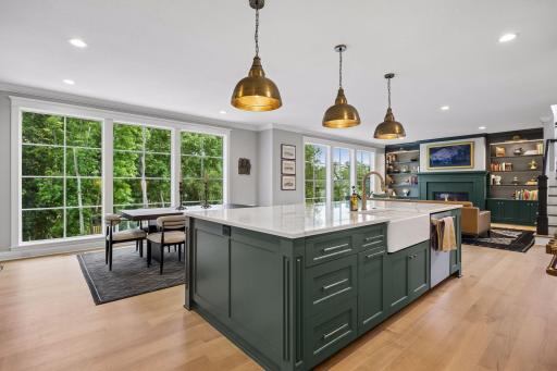 The oversized island becomes the natural gathering place, framed by panoramic woodland views beyond.