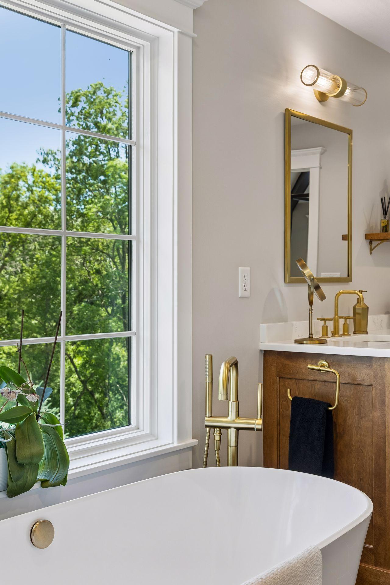 A private spa retreat where natural light pours through oversized windows, highlighting warm brass fixtures, custom millwork, and a sculptural soaking tub positioned to overlook the surrounding trees.