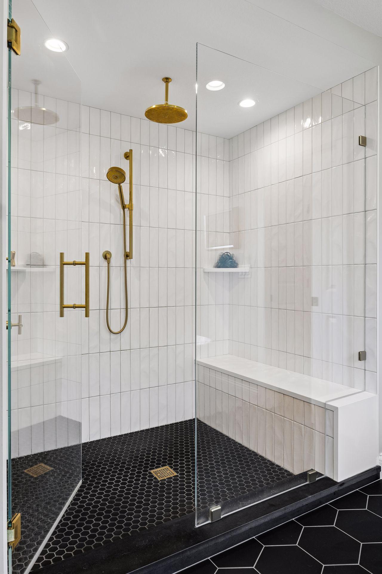 The oversized walk-in shower features full-height tile, frameless glass, bench seating, and premium brass fixtures for a true spa experience.