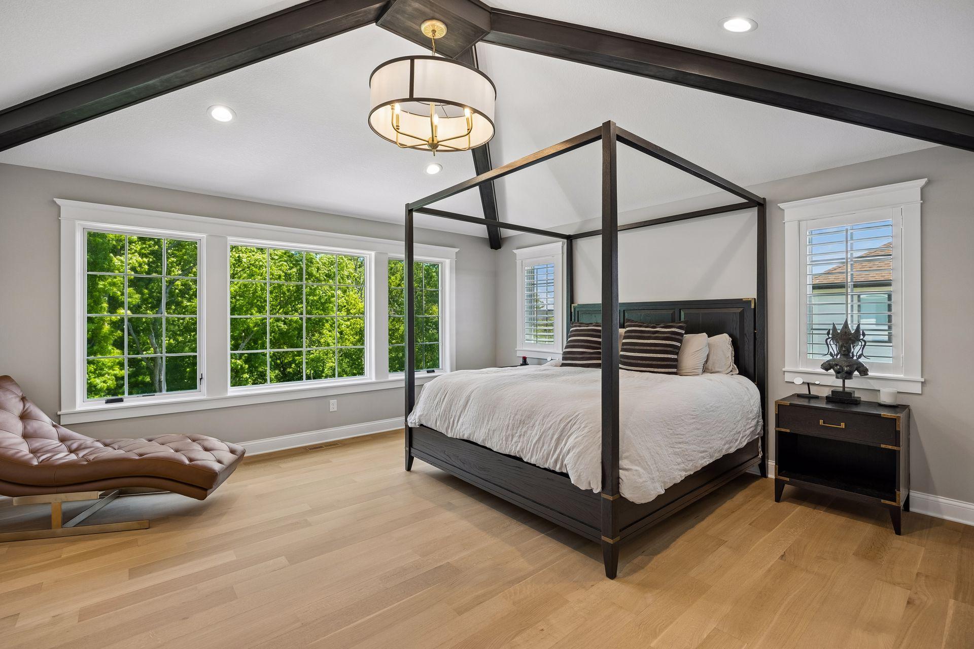 A serene owner's retreat featuring vaulted ceilings with exposed beams, expansive windows, and peaceful woodland views.
