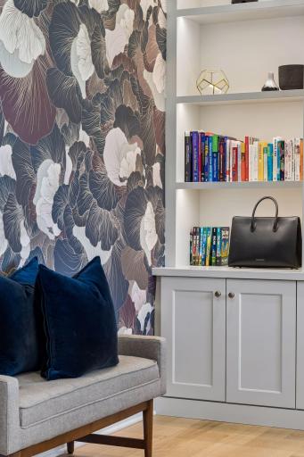 Designer wallpaper, illuminated shelving, and bespoke cabinetry create a workspace that feels equal parts library and private gallery.
