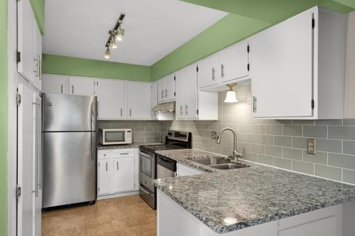 Bright kitchen with granite countertops, stainless steel appliances, subway tile backsplash, and ample cabinet and counter space.
