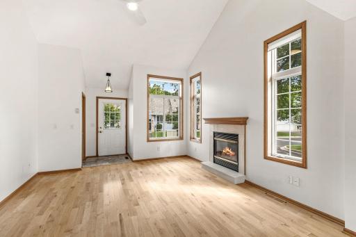 Grand two story living room with gleaming hardwood flooring and gas burning fireplace flanked by gorgeous windows.