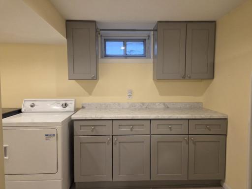 Terrific finished laundry room has loads of cabinets with hanging area in front of window.