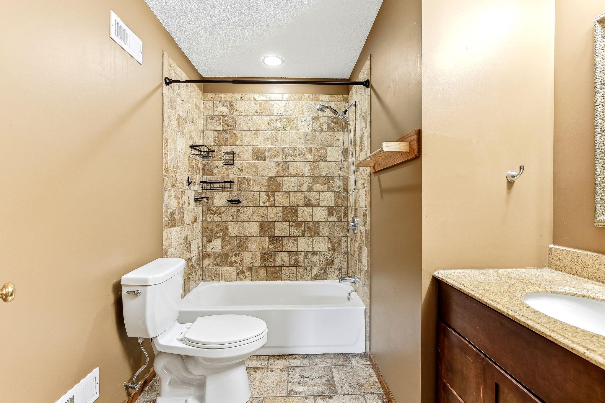 Tastefully updated bathroom with a tile-surround tub/shower, attractive vanity, and tile flooring. Neutral tones and durable finishes combine comfort, style, and easy maintenance.