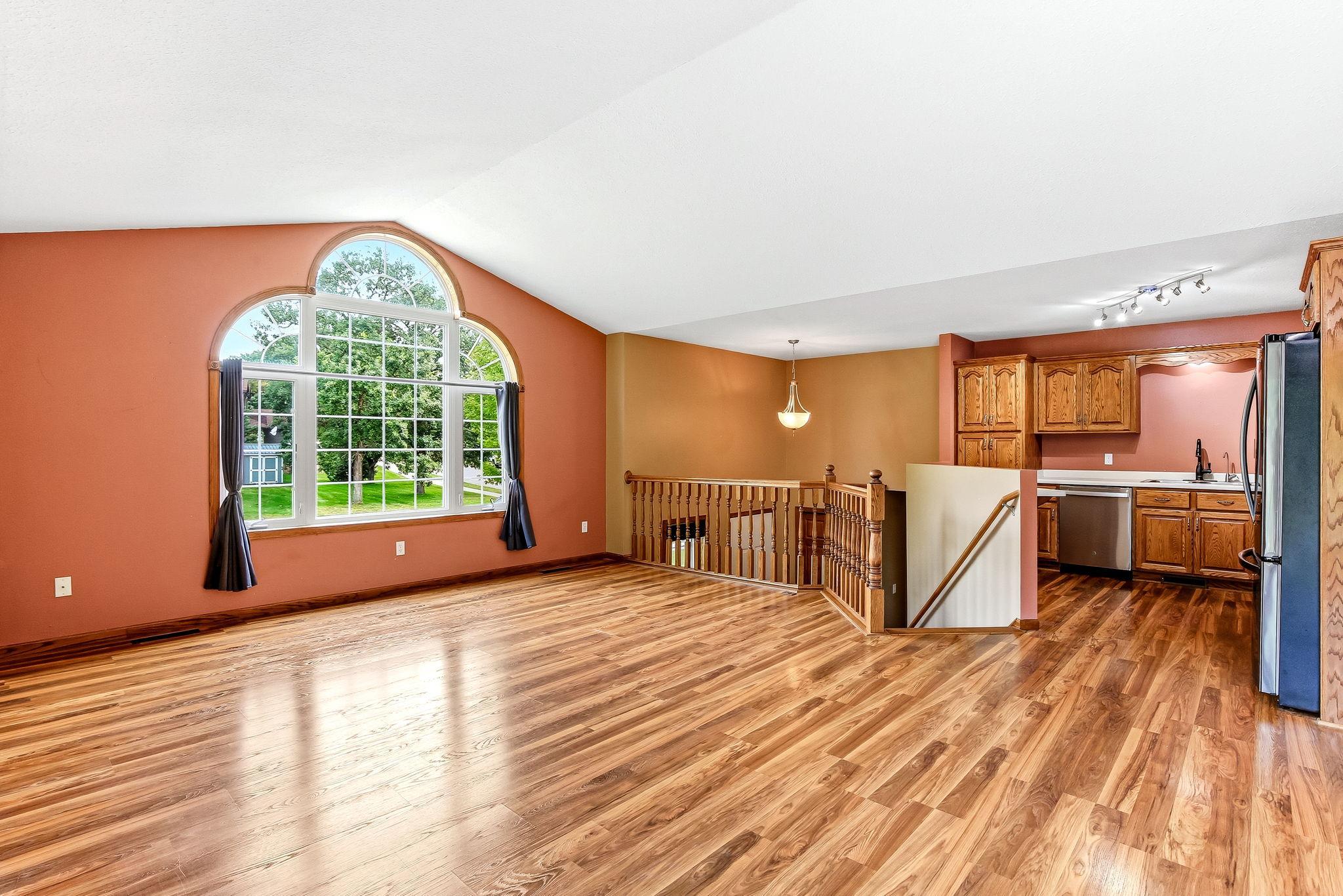 Bright and welcoming main living space featuring soaring vaulted ceilings, gleaming floors, and a stunning oversized arched window that fills the room with natural light.