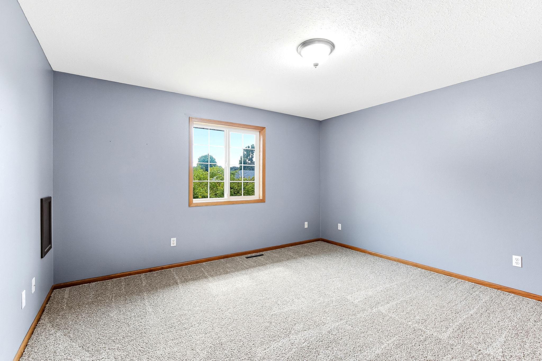 Spacious bedroom featuring plush carpeting, soft neutral tones, and a large window that fills the room with natural light. The versatile layout offers plenty of space for furnishings while creating a comfortable retreat for rest and re