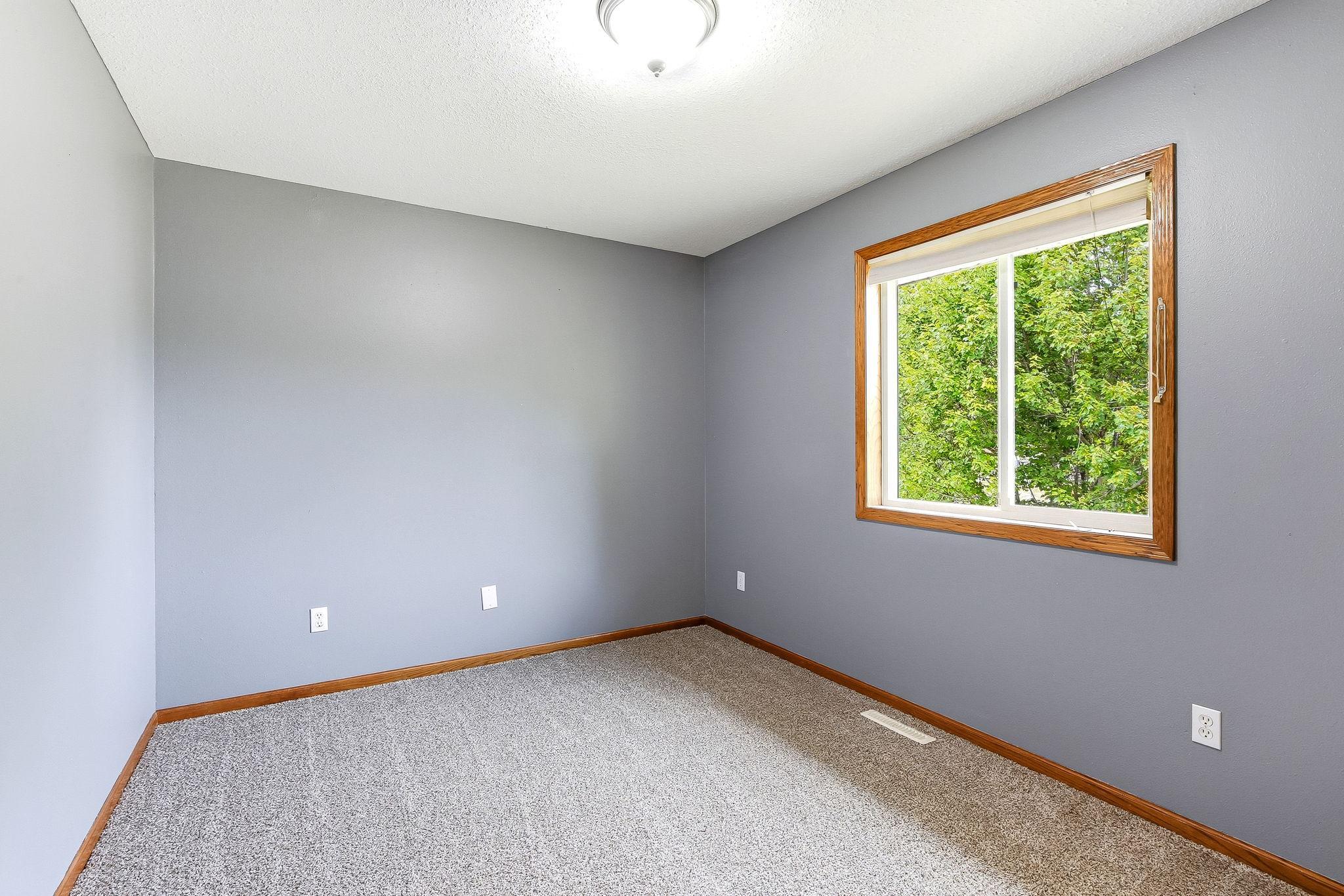 Bright secondary bedroom offering soft carpeting, generous closet space, and natural light from the large window.