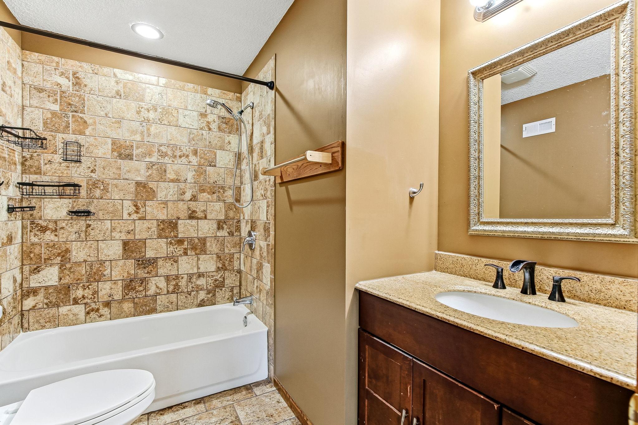 Tastefully updated bathroom with a tile-surround tub/shower, attractive vanity, and tile flooring.