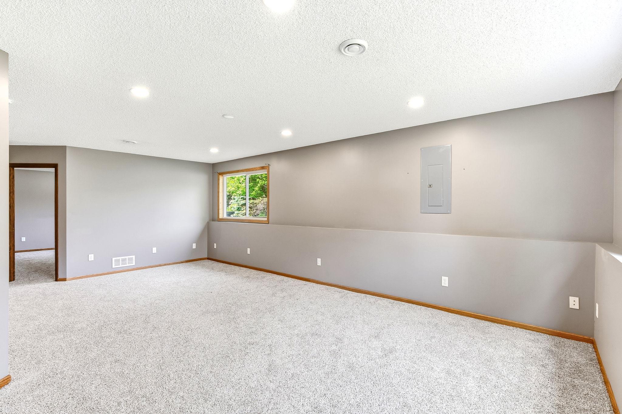 Spacious lower-level family room featuring plush new carpeting, recessed lighting, and a large window that brings in natural light.