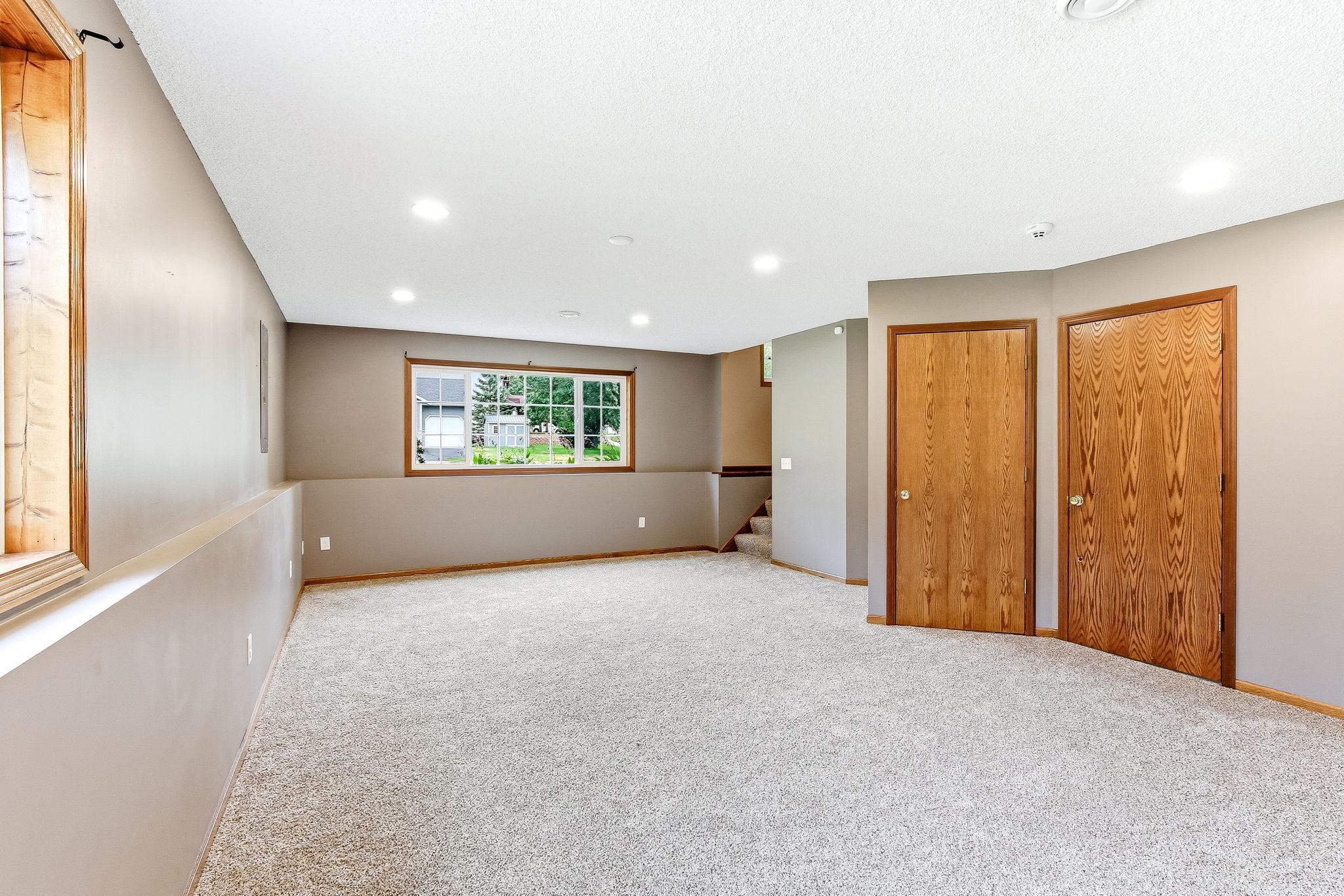 Lower-level family room featuring a large daylight window that fills the space with natural light, plush carpeting, and recessed lighting.