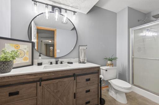 Beautifully updated lower-level bathroom featuring custom vanity, quartz-style countertop, modern fixtures, and walk-in shower.