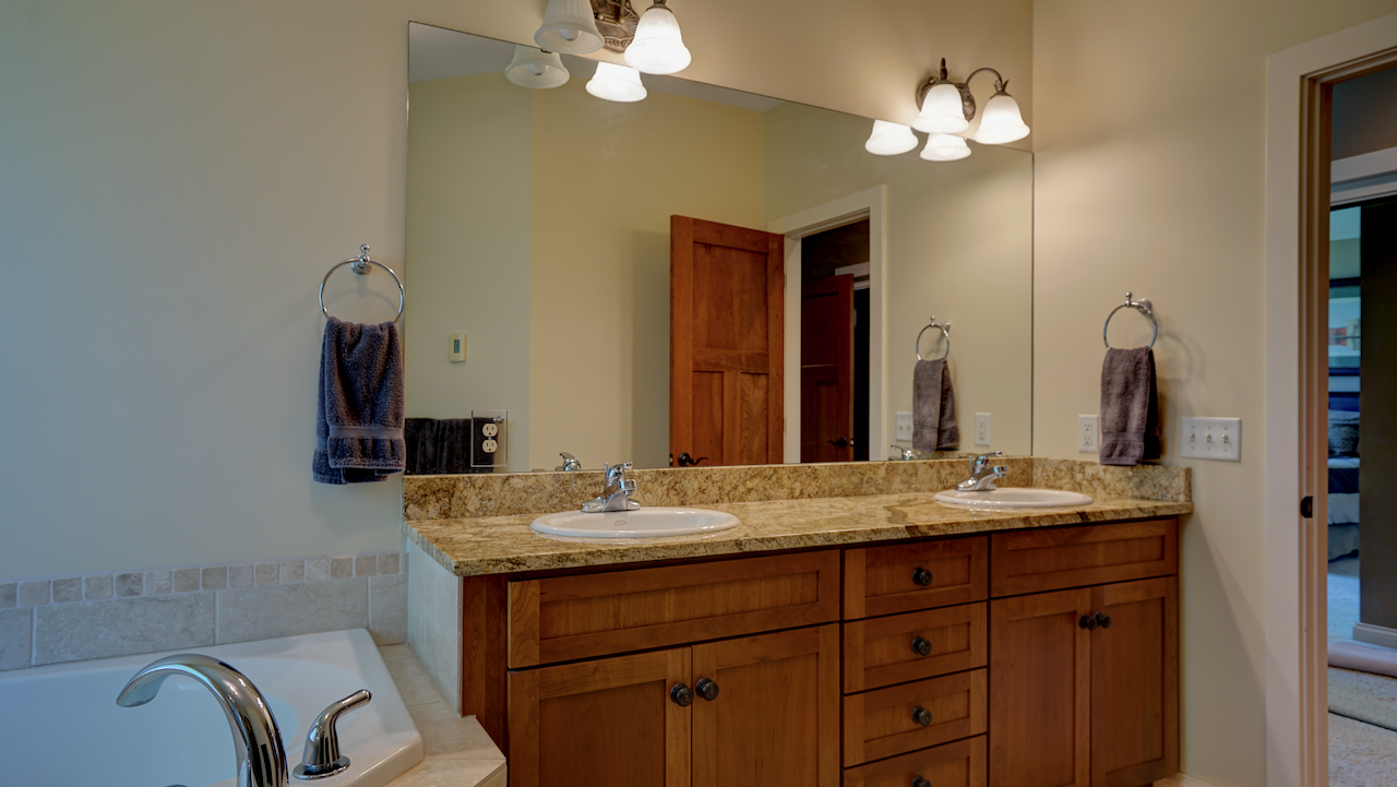 The bath features rich cherry wood cabinetry supporting a dual-sink vanity with a beautiful rustic granite countertop.