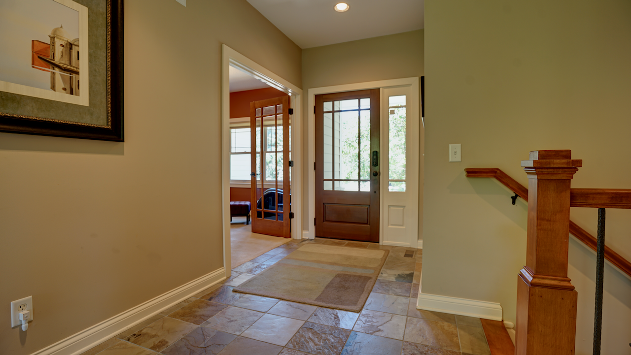 The generous vestibule creates a dedicated drop zone for guests, featuring rich maple hardwood floors that flow into the main living spaces.