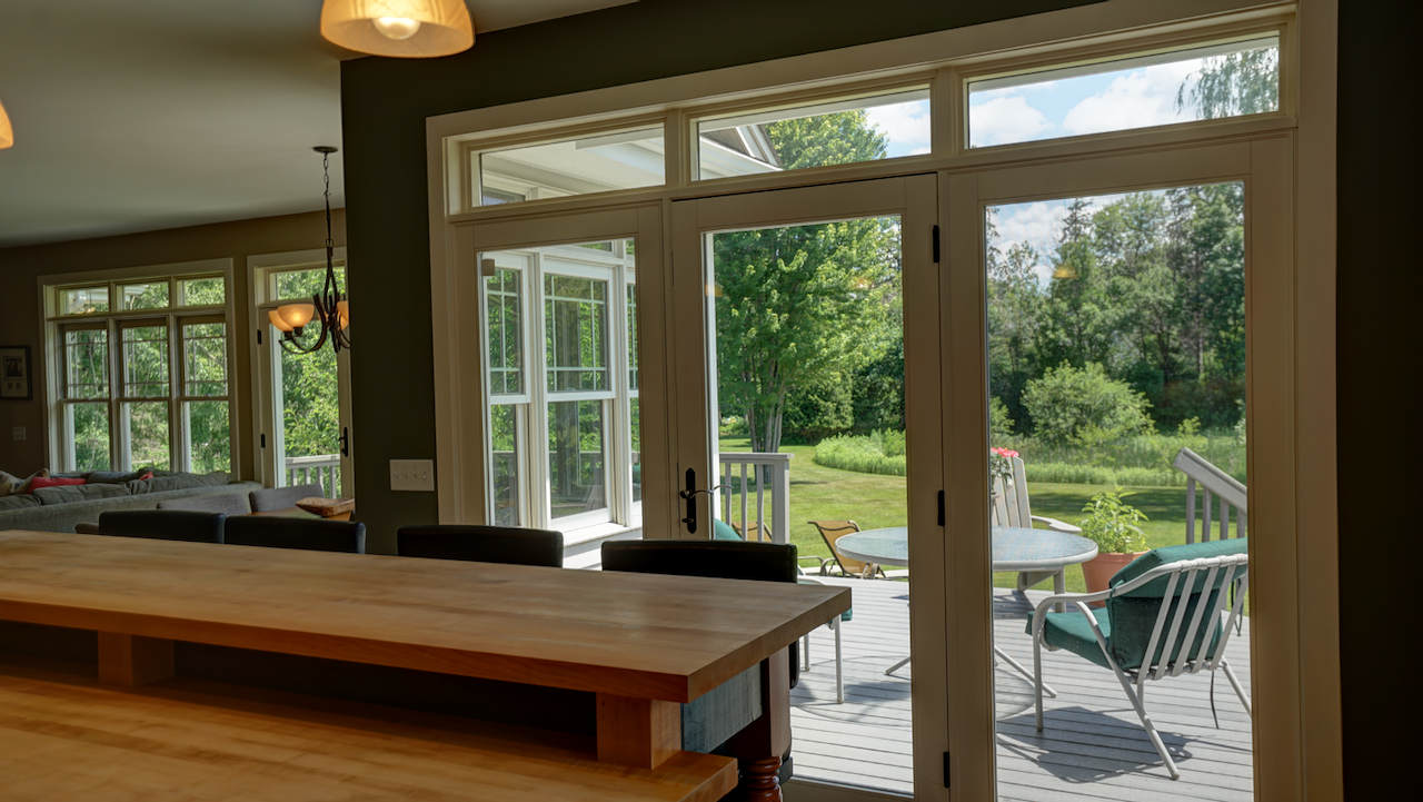 An 8-foot island anchors the room, topped with a dual-height butcher block that seats four. A triple-wide patio door with transom windows opens the dining space onto the Trex deck.