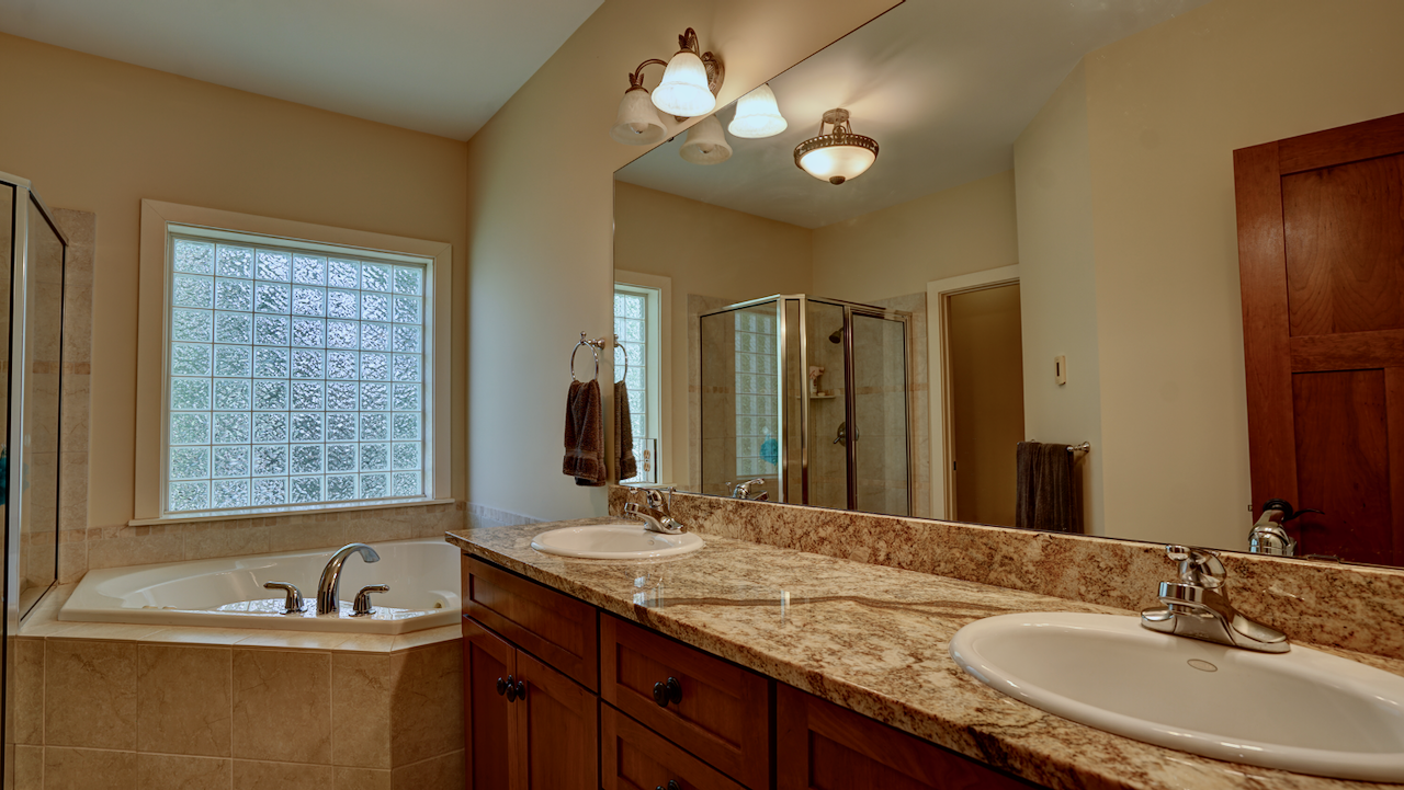 The en-suite luxury bath features rich cherry wood cabinetry supporting a dual-sink vanity with a beautiful rustic granite countertop.