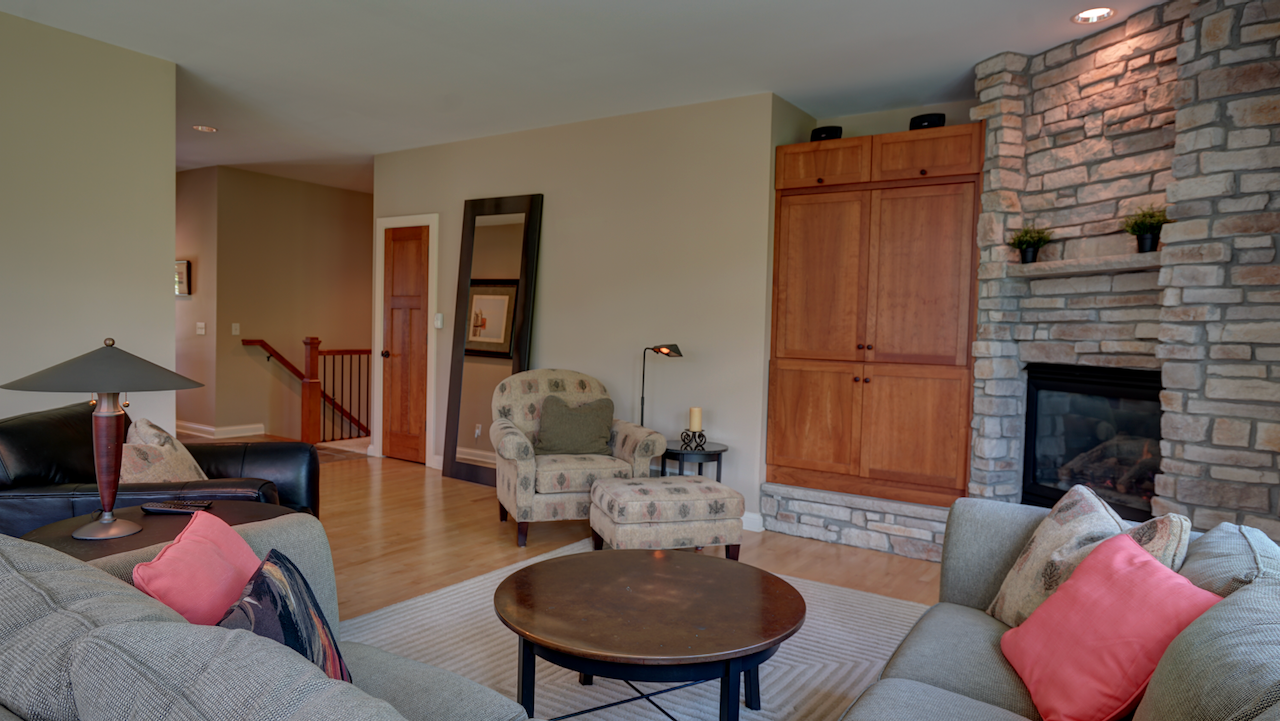 Looking across the living room showing the built-in entertainment center attractive gas fireplace with floor to ceiling custom stone. In the distance you can see the wide stairwell to the lower level and hallway to the bedrooms.