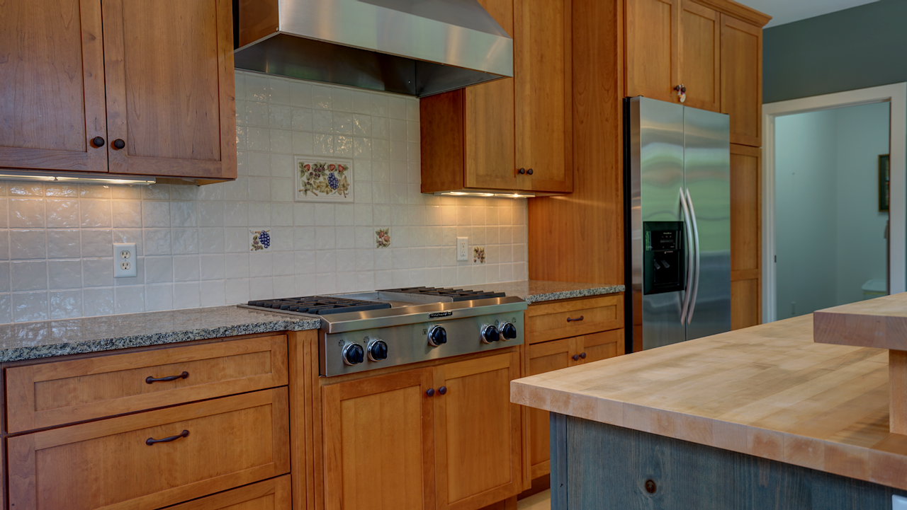 The chef’s workspace includes a built-in KitchenAid gas cooktop with an integrated central griddle and an overhead ventilation hood.Solid granite perimeter countertops provide extensive prep space, under-cabinet lighting and a light tile backsplash.