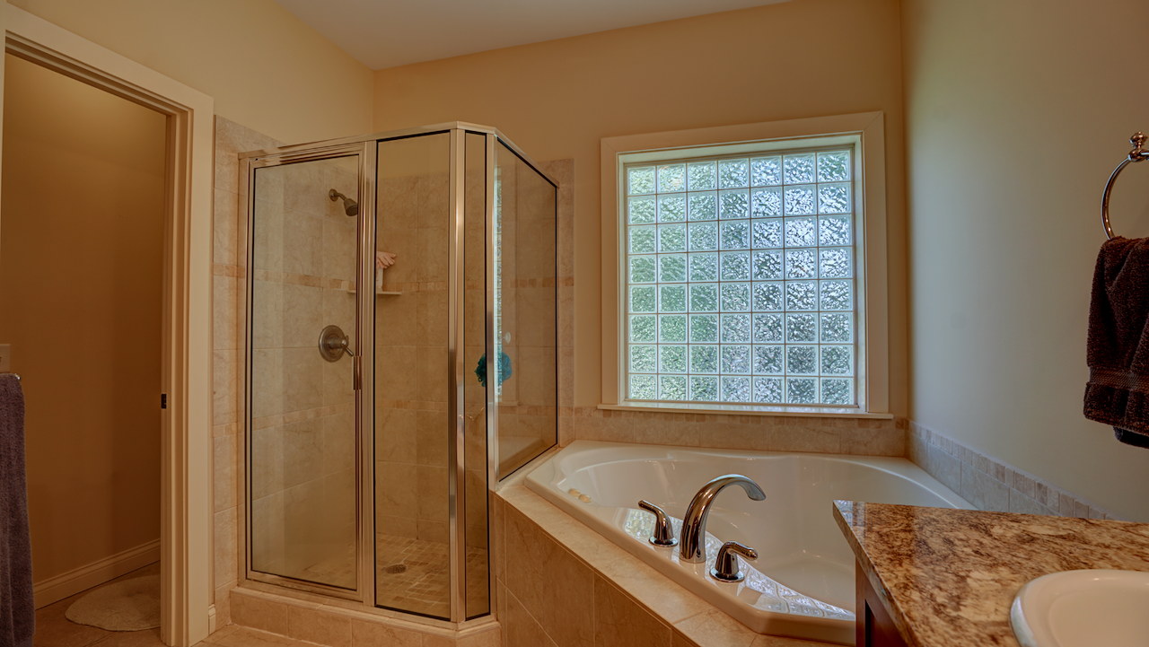 A step-up corner whirlpool soaking tub creates a spa-like atmosphere, perfect for unwinding after a long day. The primary bath is completed by a custom fully tiled walk-in shower and a separate enclosed privacy toilet area.