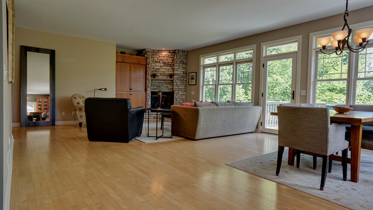 Viewed from the kitchen, the open floor plan highlights the scale of the main level. Maple hardwood floors carry the eye straight to the stone gas fireplace and cherry built-ins in the living area