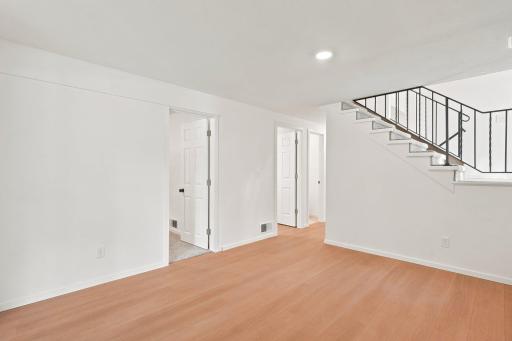 Lower level family room area with door on left to 3rd bedroom and doors on right to utility/laundry room and next door is lower level 1/2 bathroom.
