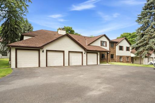 Front elevation featuring an attached one-car garage, additional detached garage stalls, mature trees, and a well-maintained community setting.