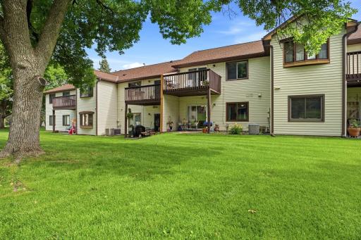 Rear exterior showcasing the building, private patios and decks, and expansive shared green space with mature trees