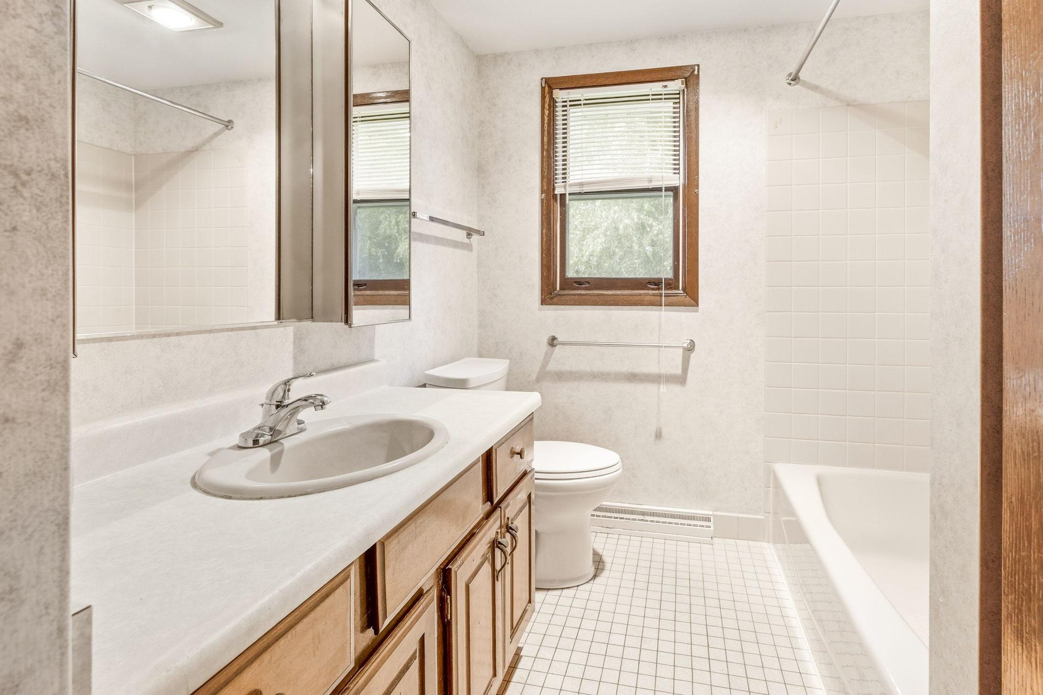 Full bathroom featuring a large vanity, tub/shower combination, and a window that fills the space with natural light.