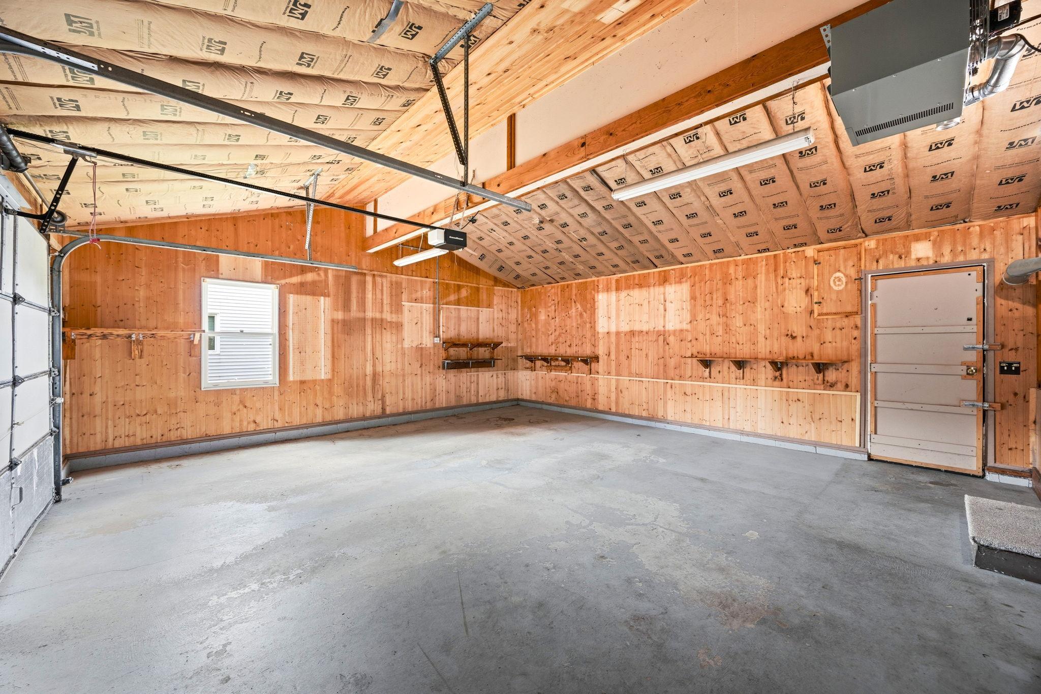 Oversized insulated garage with vaulted ceilings, built in shelving, and plenty of room for parking, storage, or a workshop