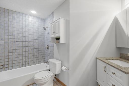 Clean and functional bathroom with a tub-and-shower combo, tiled walls, a standard white toilet, and a wall-mounted storage cabinet for extra convenience.