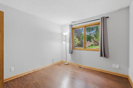Bright and inviting bedroom or home office with natural wood trim, laminate flooring, and a large window that floods the space with natural light.