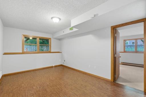 Spacious and bright finished basement recreation room with neutral white walls, warm wood-look flooring, and egress windows for plenty of daylight.