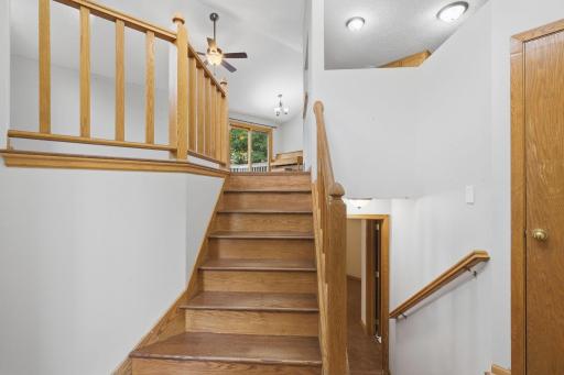 Welcoming entryway and split-level staircase featuring solid wood railings, bright overhead lighting, and transitions to both the upper and lower levels.