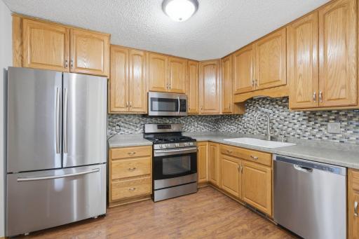 Modern kitchen featuring classic oak cabinetry and a tile backsplash. Equipped with stainless steel appliances, including a built-in microwave, gas range, and refrigerator.